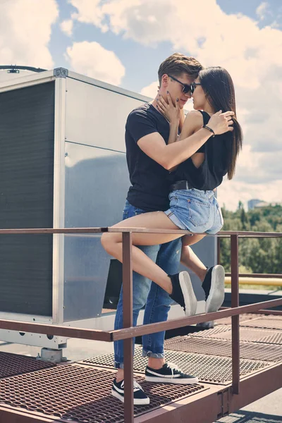 Multicultural casal quente abraçando e indo para beijar em grades no telhado — Fotografia de Stock