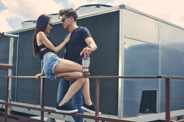 Schönes junges multikulturelles Paar flirtet und hält eine Flasche Whiskey auf dem Dach — Stockfoto