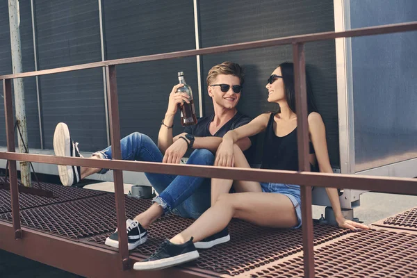 Asian girlfriend and caucasian boyfriend with bottle of rum spending time together on roof — Stock Photo