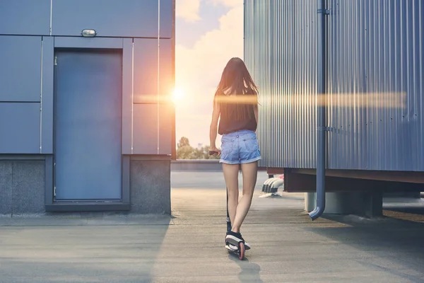 Back view of young woman riding scooter on roof with sunbeams — Stock Photo