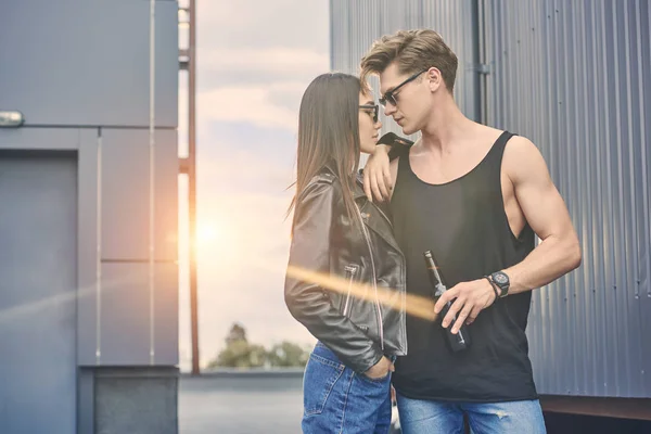 Casal interracial com garrafa de cerveja abraçando no telhado com backlit — Fotografia de Stock