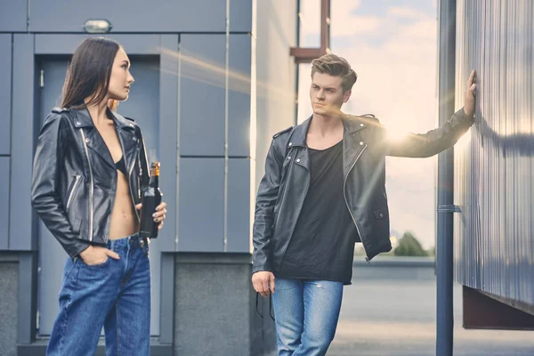 Asian girl with bottle of beer looking at stylish man standing on roof with sunlight — Stock Photo