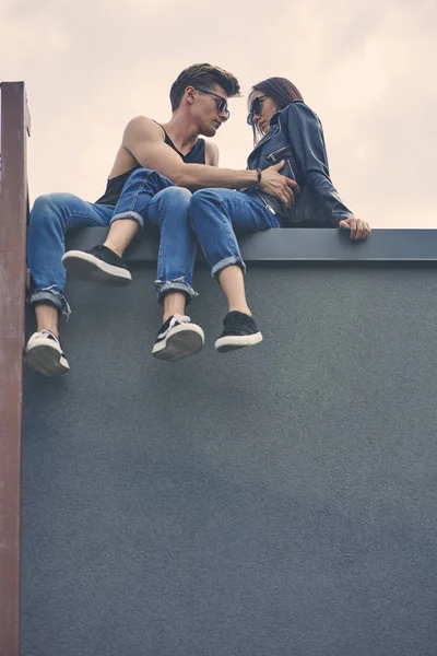 Вид снизу на стильную межрасовую пару флиртующую и обнимающуюся на крыше — стоковое фото