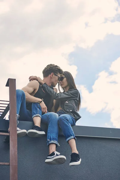 Bottom view of multicultural couple embracing while sitting on roof — Stock Photo