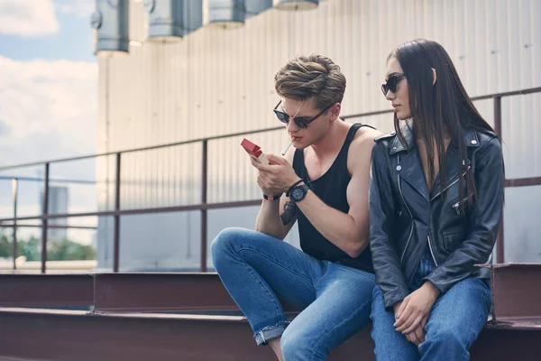 Joven elegante hombre fumar cigarrillo cerca de su asiático novia - foto de stock