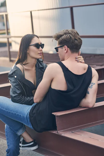 Interrazziale caldo coppia in occhiali da sole abbracciare e guardando ogni altro su urbano tetto — Foto stock