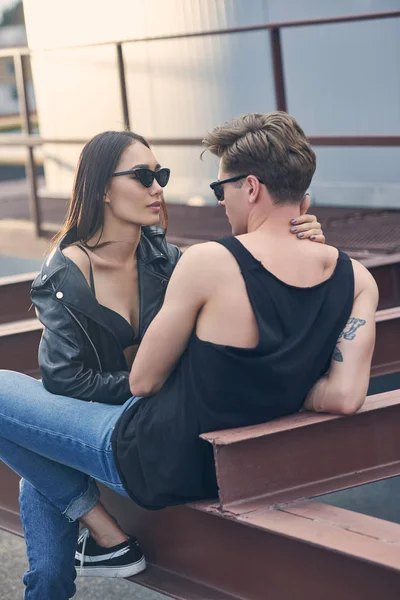 Interracial couple chaud dans des lunettes de soleil étreignant et se regardant sur le toit urbain — Photo de stock