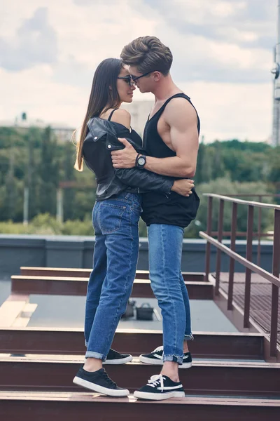 Couple chaud élégant multiethnique dans des lunettes de soleil embrassant et allant embrasser sur le toit urbain — Photo de stock