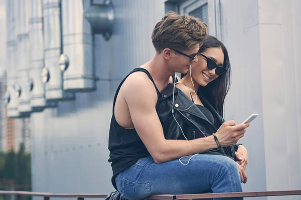 Smiling interracial couple listening music with earphones and using smartphone — Stock Photo