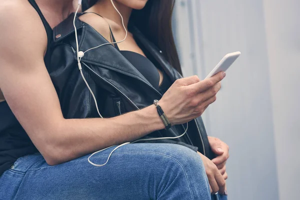 Vue recadrée d'un couple élégant écoutant de la musique avec des écouteurs et utilisant un smartphone — Photo de stock