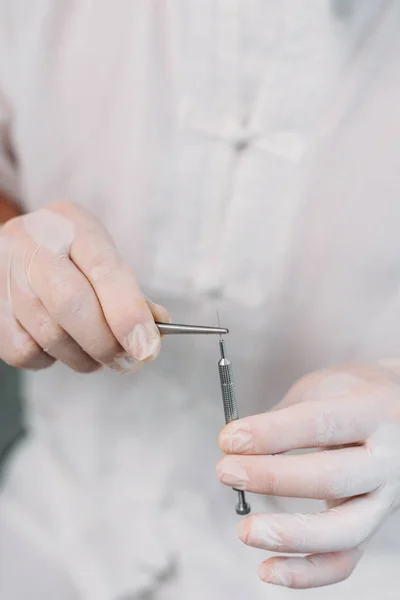 Vista parcial del cosmetólogo en bata blanca y guantes de látex que sostienen la aguja para la terapia de acupuntura - foto de stock