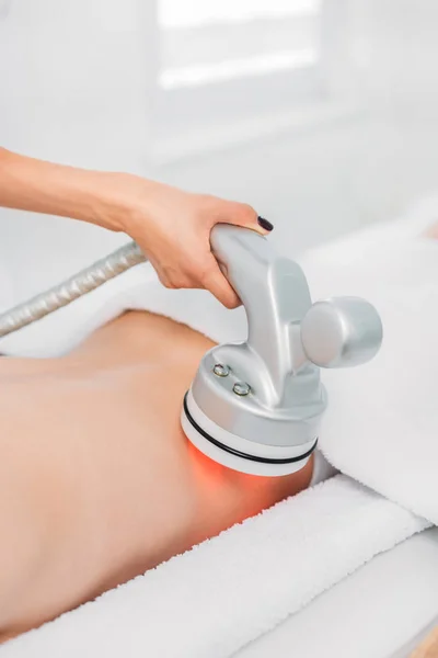 Tiro recortado de la mujer en la mesa de masaje recibiendo masaje eléctrico hecho por el cosmetólogo en el salón de spa - foto de stock