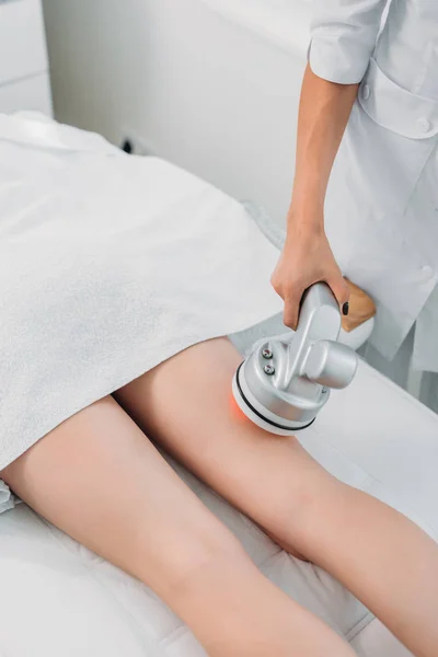 Vista parziale della donna sul tavolo da massaggio ottenere massaggio elettrico fatto da cosmetologo nel salone spa — Foto stock