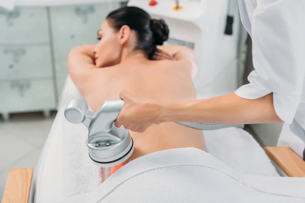 Mujer en la mesa de masaje recibiendo masaje eléctrico hecho por el cosmetólogo en el salón de spa - foto de stock
