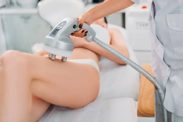 Частичный взгляд косметолога, делающего электрический массаж клиентке в белом нижнем белье в спа-салоне — стоковое фото