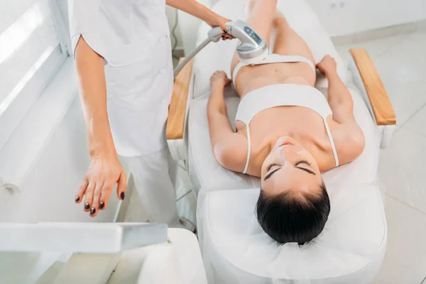 Atractiva mujer recibiendo masaje eléctrico hecho por el cosmetólogo en el salón de spa - foto de stock