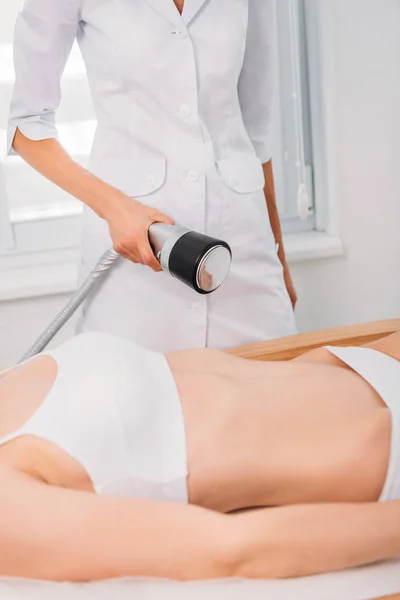 Cropped shot of cosmetologist making electrical massage to female client in white underwear in spa salon — Stock Photo