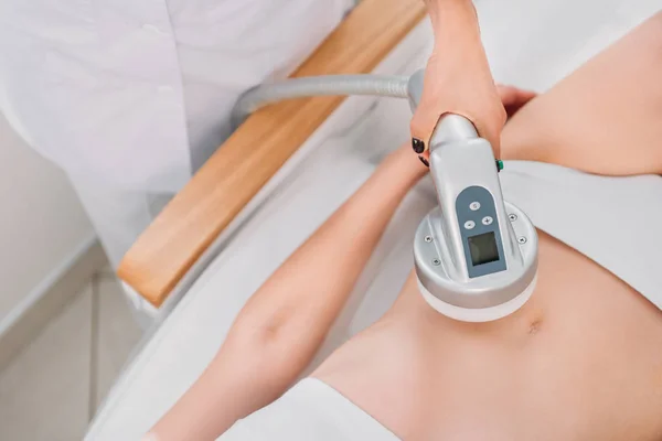 Partial view of cosmetologist making electrical massage to female client in white underwear in spa salon — Stock Photo