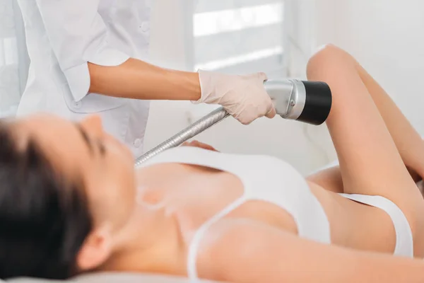 Partial view of cosmetologist making electric massage on leg to woman in white underwear at spa salon — Stock Photo