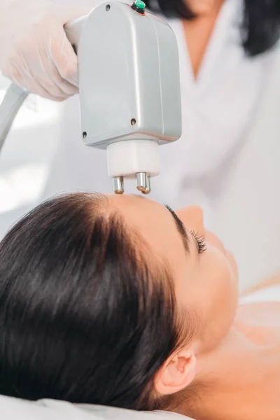 Vue partielle de la femme obtenant massage électrique stimulant du visage faite par le cosmétologue dans le salon de spa — Photo de stock