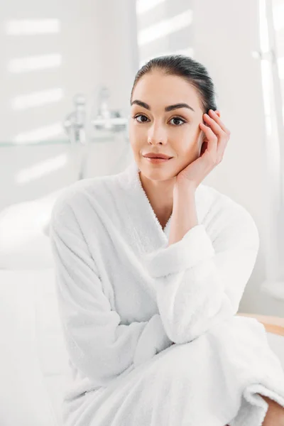 Retrato de hermosa mujer en albornoz blanco sentado en la mesa de masaje en el salón de spa - foto de stock