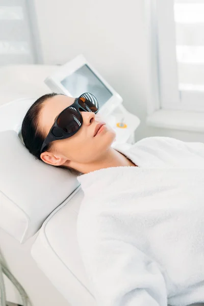 Mujer en gafas protectoras consiguiendo depilación láser hecha por cosmetólogo en salón de spa - foto de stock