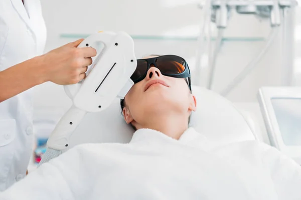 Woman in protective eyeglasses getting laser hair removal made by cosmetologist in spa salon — Stock Photo