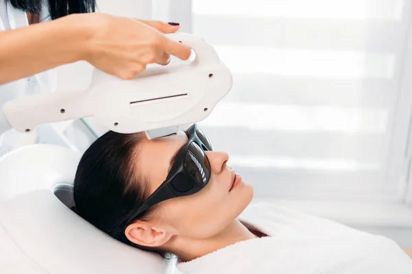 Woman in protective eyeglasses getting laser hair removal made by cosmetologist in spa salon — Stock Photo