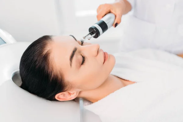 Atractiva mujer recibiendo terapia de microcorriente facial en el salón de spa - foto de stock