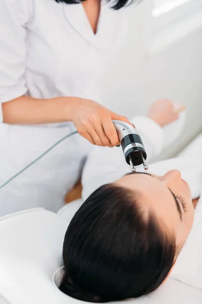 Atractiva mujer recibiendo terapia de microcorriente facial en el salón de spa - foto de stock