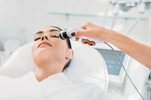 Atractiva mujer recibiendo terapia de microcorriente facial en el salón de spa - foto de stock