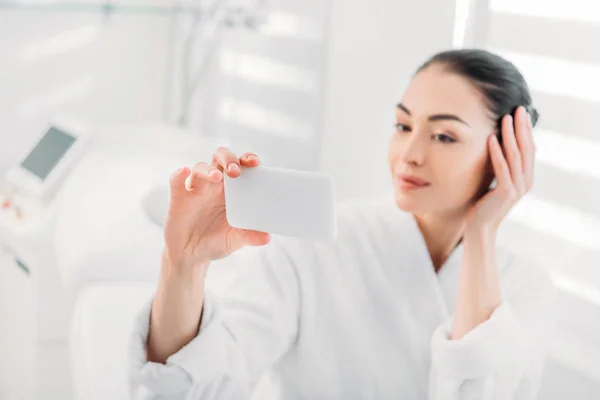 Femme en peignoir blanc prenant selfie sur smartphone dans le salon de spa — Photo de stock