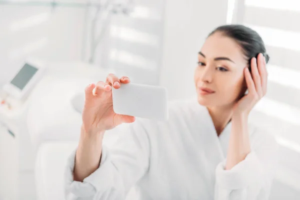 Mulher de roupão branco tomando selfie no smartphone no salão de spa — Fotografia de Stock