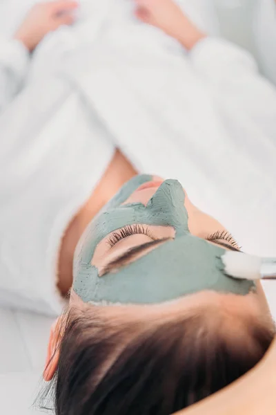 Teilansicht des Kosmetikers, der im Wellness-Salon Tonmaske auf das weibliche Gesicht aufträgt — Stockfoto