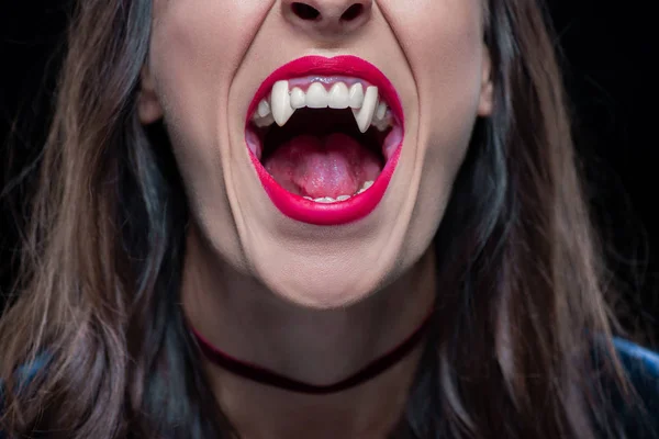 Обрезанный вид женщины, показывающей вампирские клыки изолированные на черном — стоковое фото