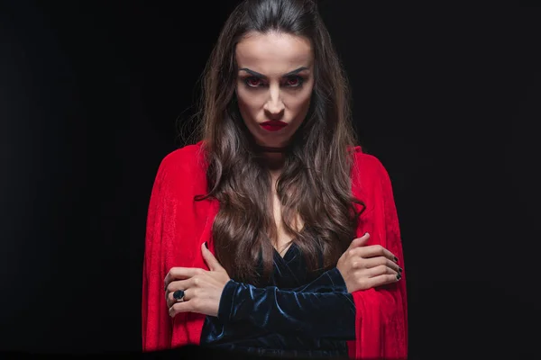 Grim vampire woman in red cloak looking at camera isolated on black — Stock Photo