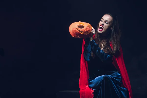 Mystery woman in vampire costume holding jack o lantern on dark background — Stock Photo