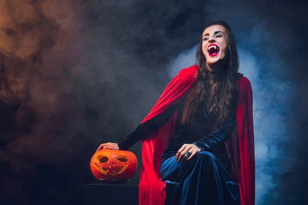 Hermosa mujer en traje de vampiro sonriendo sobre fondo oscuro con humo - foto de stock