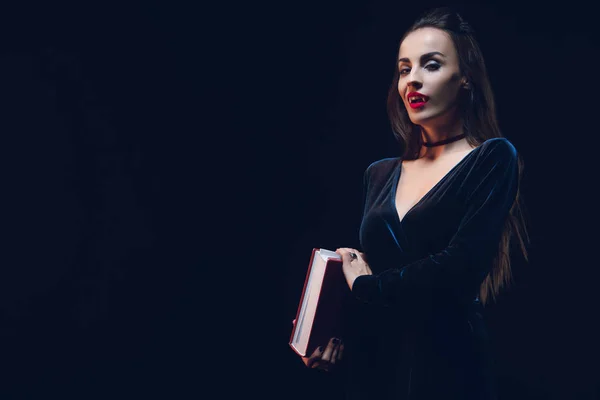 Beautiful vampire woman holding magic book isolated on black — Stock Photo