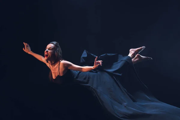 Mujer espantosa en traje de vampiro volando sobre fondo oscuro - foto de stock