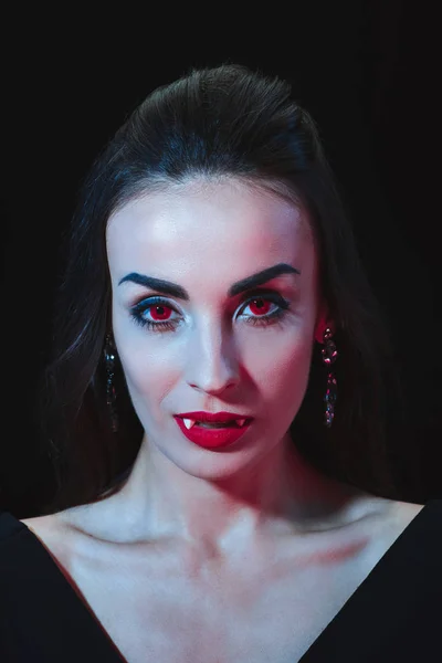 Сексуальная женщина-вампир с красными глазами, смотрящая на камеру, изолированную на черном — стоковое фото