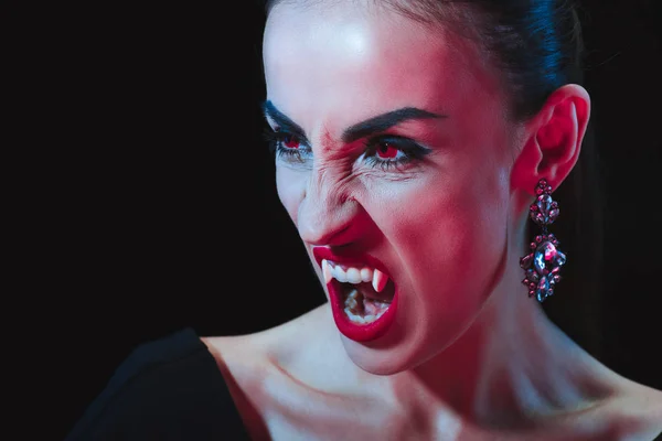 Dreadful vampire showing her fangs and looking away isolated on black — Stock Photo