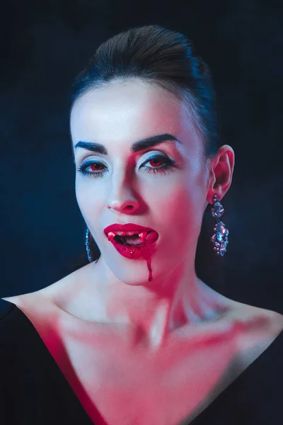 Sexy vampiro mujer lamiendo sus labios en oscuro fondo - foto de stock