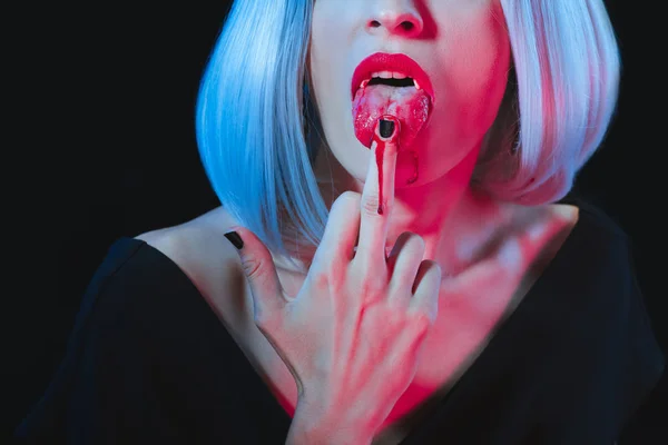 Abgeschnittene Ansicht von Vampirfrau leckt ihren Mittelfinger isoliert auf schwarz — Stockfoto