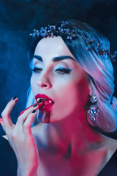 Sexy vampiro donna leccare il sangue dalle dita su sfondo scuro con il fumo — Foto stock