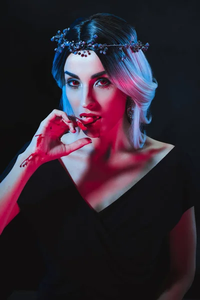 Vampire woman licking bloody fingers isolated on black — Stock Photo