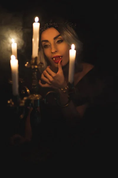 Attraktive Frau im Vampirkostüm leckt ihre Finger mit Leuchter im Vordergrund — Stockfoto