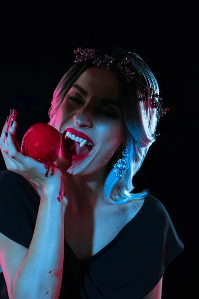 Hermosa vampiro mujer mordiendo rojo sangriento manzana aislado en negro - foto de stock