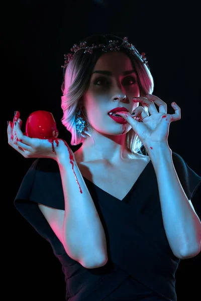 Vampiro mujer con rojo sangriento manzana lamiendo sus dedos aislado en negro - foto de stock