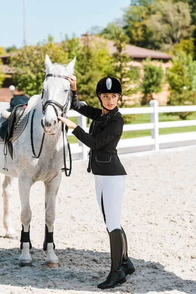 Attractive female equestrian fixing horse halter and looking away at horse club — Stock Photo